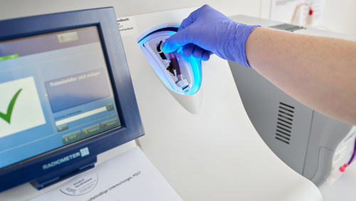 Mann mit Handschuh führt Gefäß mit Blutprobe in ein modernes Messgerät